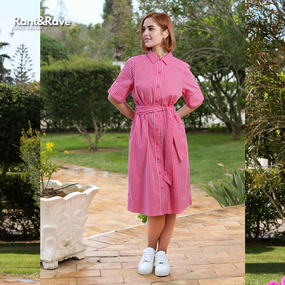 Woman wearing a pink striped dress standing outdoors on a patio with greenery.
