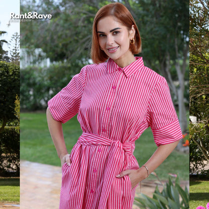 Woman wearing a pink and white striped dress standing outdoors with greenery in the background