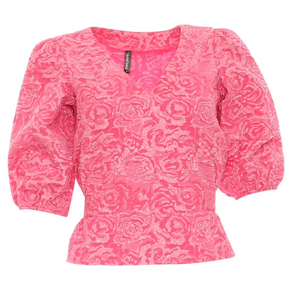 A bright pink short-sleeve blouse with a textured rose pattern, featuring a V-neckline and puffed sleeves, shown against a plain white background.