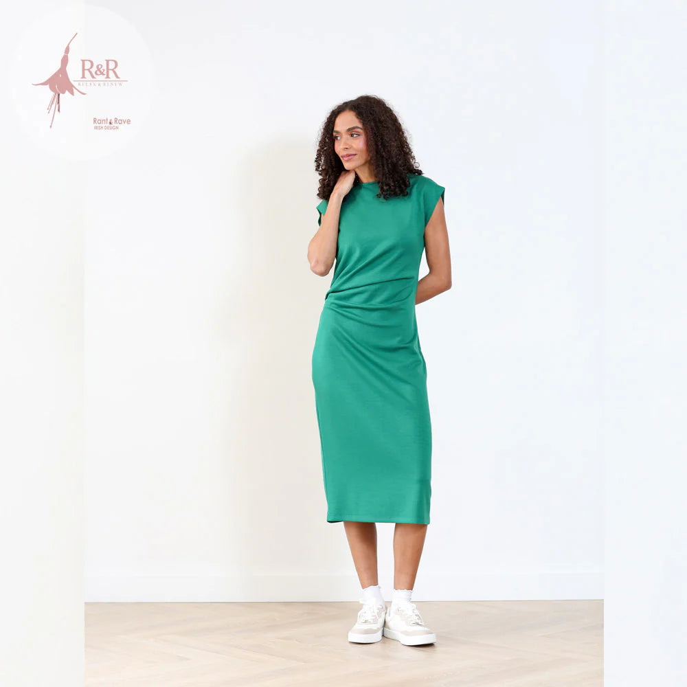 Woman wearing a green dress standing against a white background with 'R&R' branding.