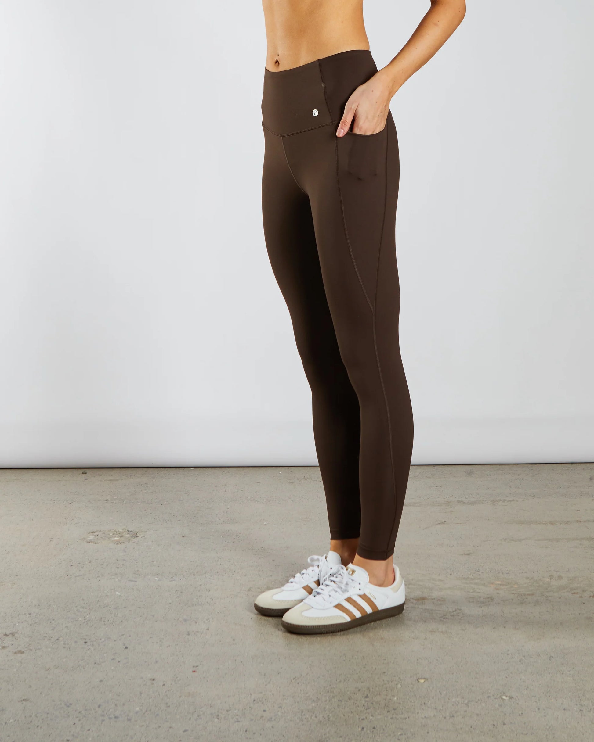 Person wearing brown leggings with white sneakers on a plain background