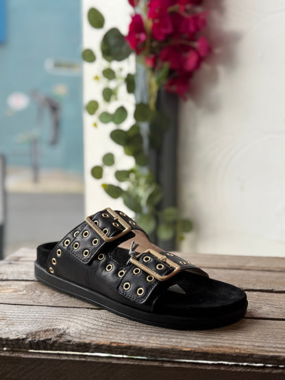 Black sandal with gold buckles on a wooden surface with a blurred background