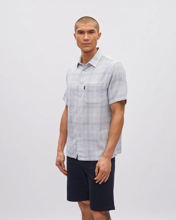 Man wearing a checkered shirt and dark shorts against a white background
