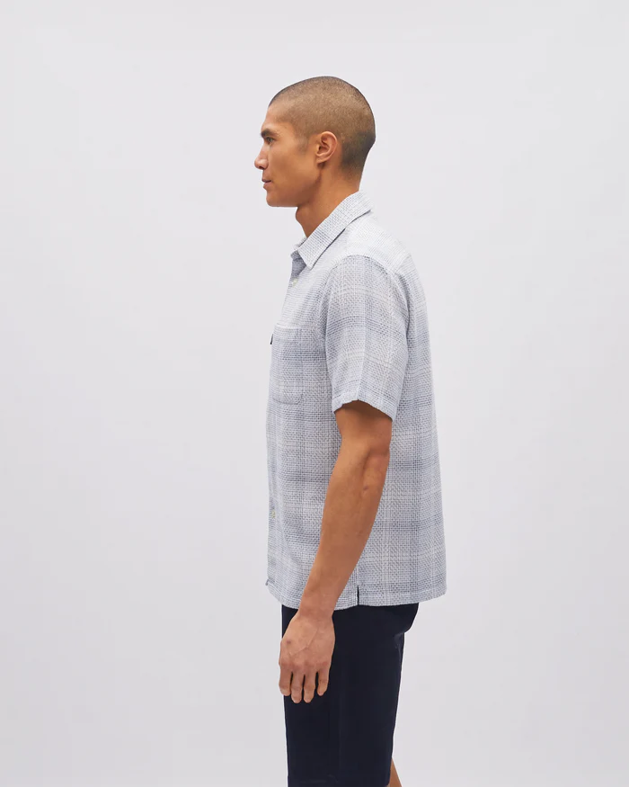 Man wearing a checkered shirt standing against a plain background