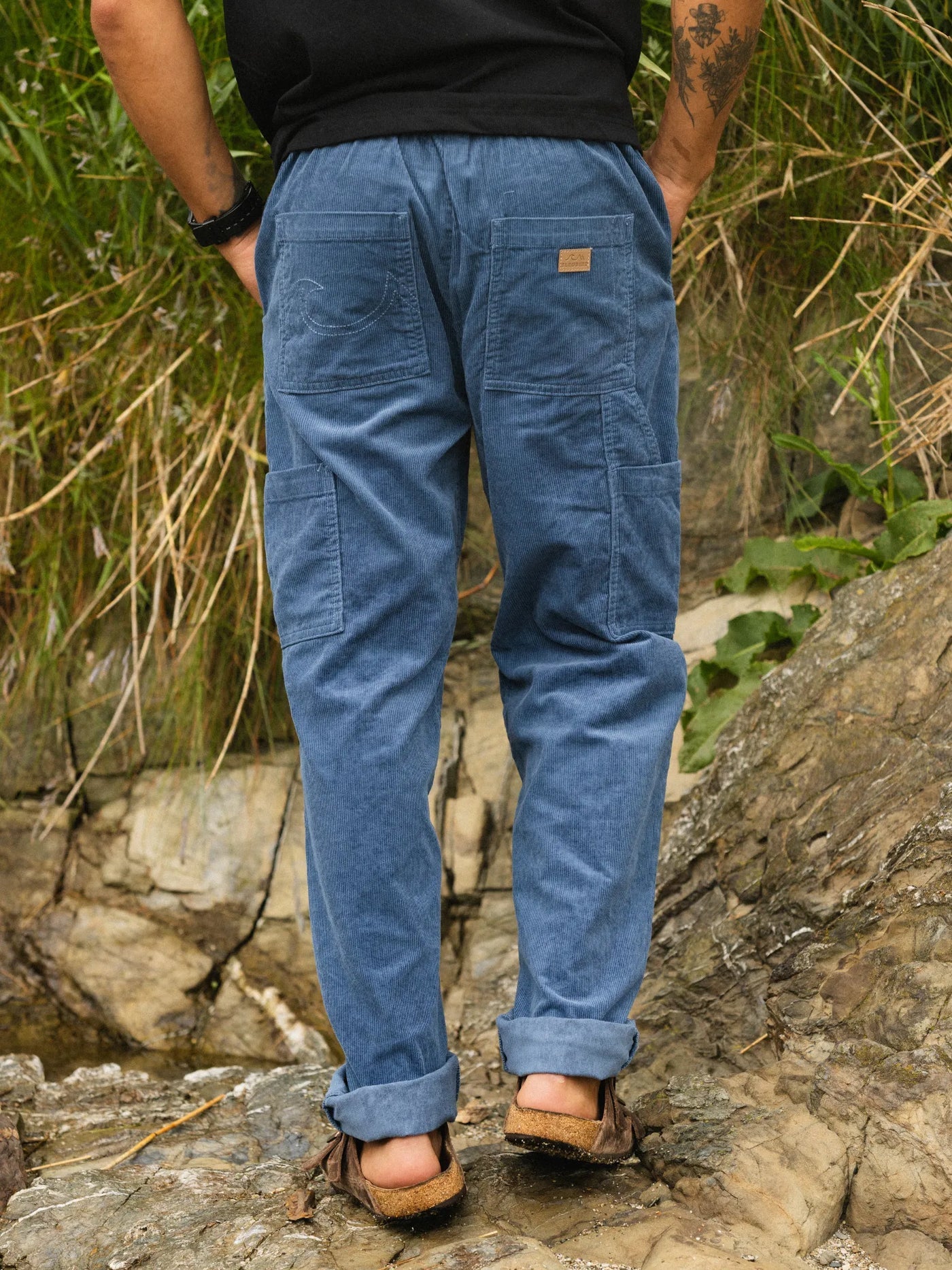 Person wearing blue pants standing on a rocky terrain with greenery in the background