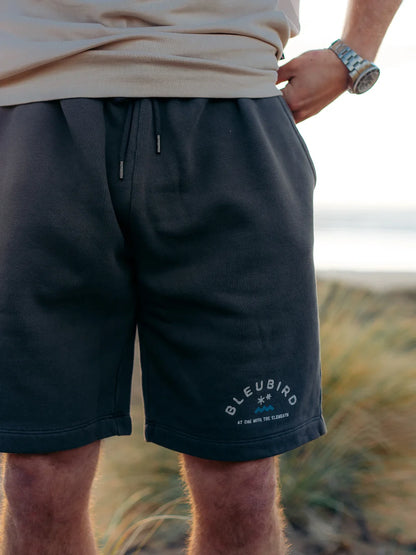 Person wearing black shorts with 'BLEUBIRD' branding in a natural setting.
