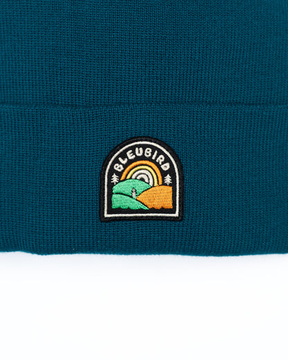 Close-up of a teal beanie with a embroidered logo on a white background