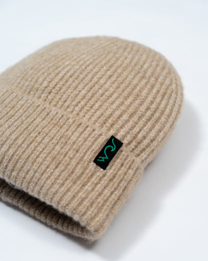 Beige knit beanie with a black and green logo on a white background
