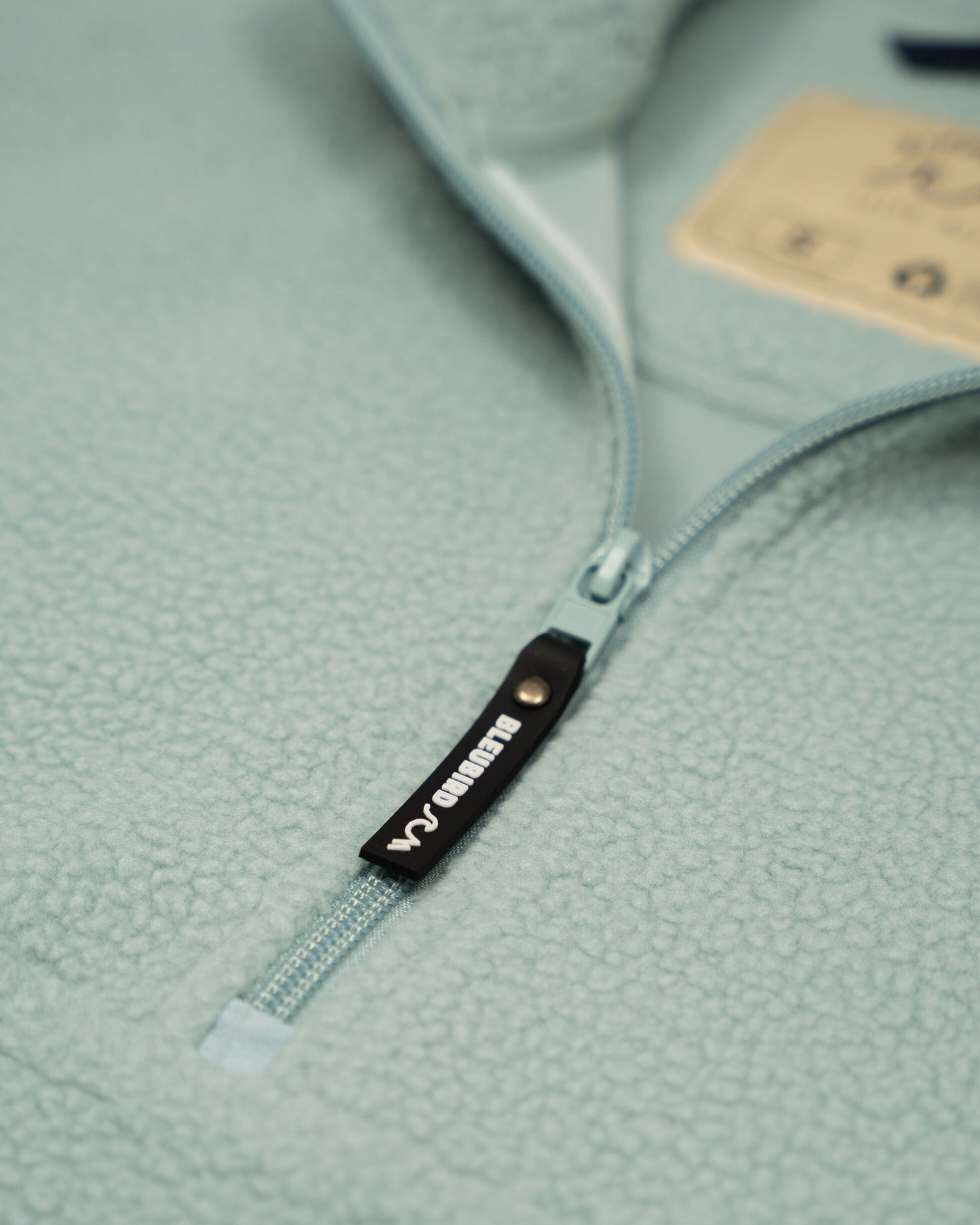 Close-up of a zipper on a light green garment with a brand label.