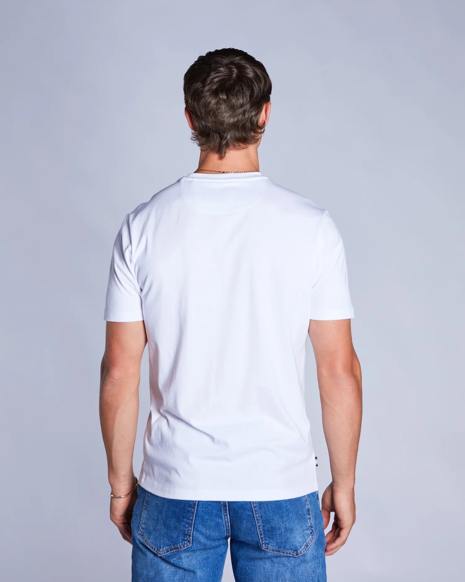 Man wearing a plain white t-shirt and blue jeans against a light gray background