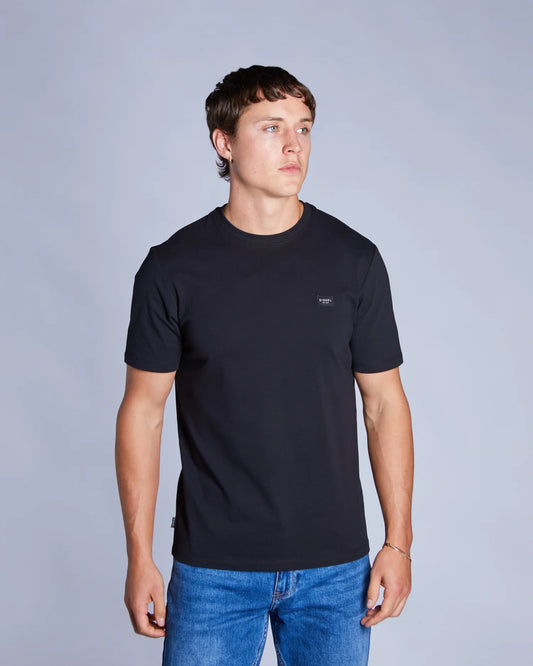 Man wearing a black t-shirt with a small logo on a gray background