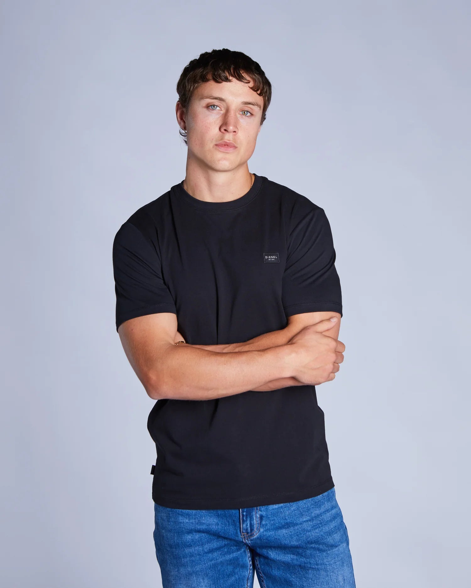 Man wearing a black t-shirt and blue jeans against a gray background