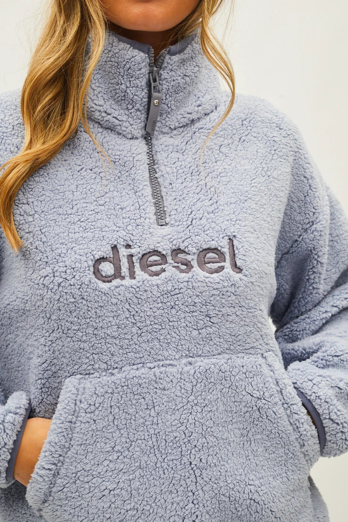 A close-up of a person wearing a light blue sherpa fleece quarter-zip pullover sweatshirt with the brand name 'diesel' embroidered across the chest.