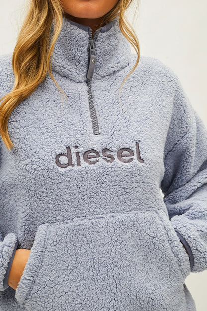 A close-up of a person wearing a light blue sherpa fleece quarter-zip pullover sweatshirt with the brand name 'diesel' embroidered across the chest.