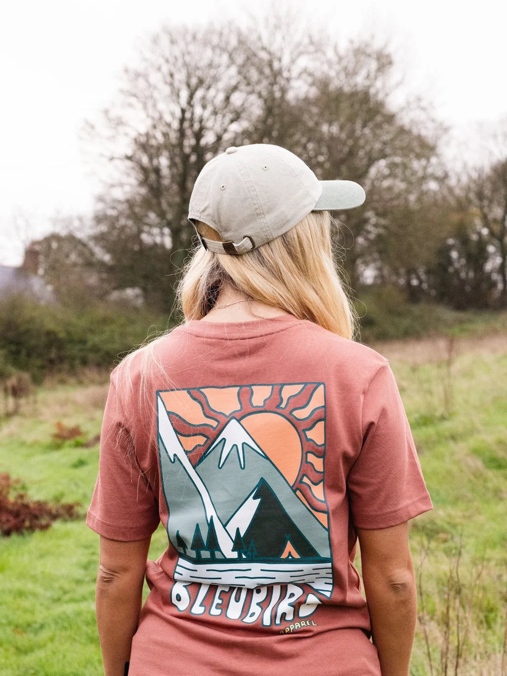 Person wearing a pink t-shirt with a mountain design in a natural setting
