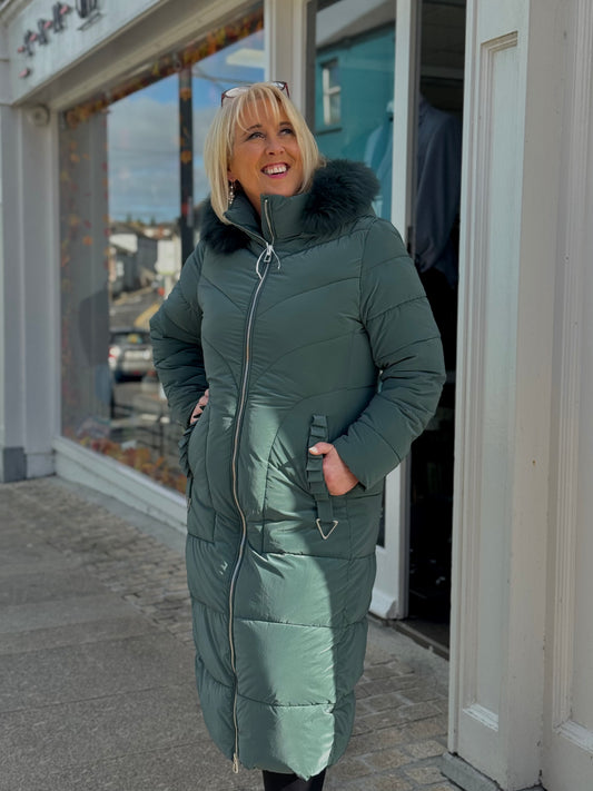 Woman wearing a green puffer coat with a fur-lined hood standing outside a store.