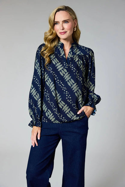 A woman modeling a navy blue long-sleeve blouse with a beige and white geometric pattern, paired with dark blue wide-leg pants, against a neutral gray studio background.