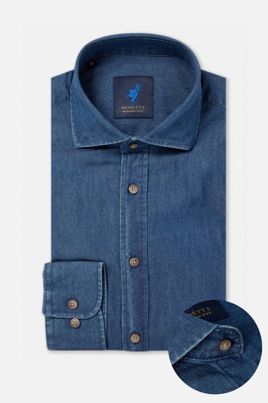 A folded blue denim long-sleeve dress shirt with a button-down front, pointed collar, and a cuff detail inset showing the button and brand label.