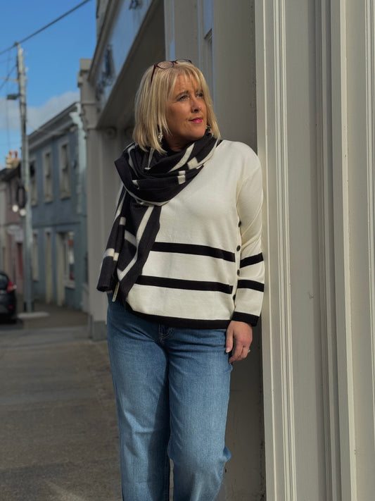 Woman wearing a striped sweater and scarf standing on a street corner.
