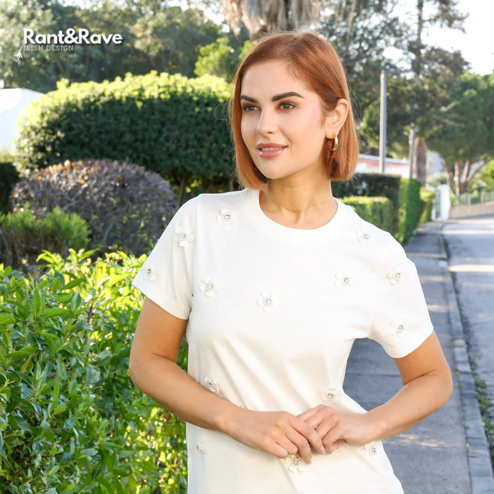 Woman in a white outfit standing outdoors with greenery in the background