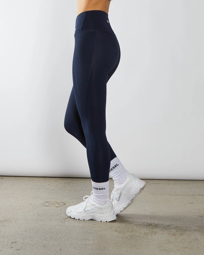 Person wearing navy leggings and white sneakers on a light gray background