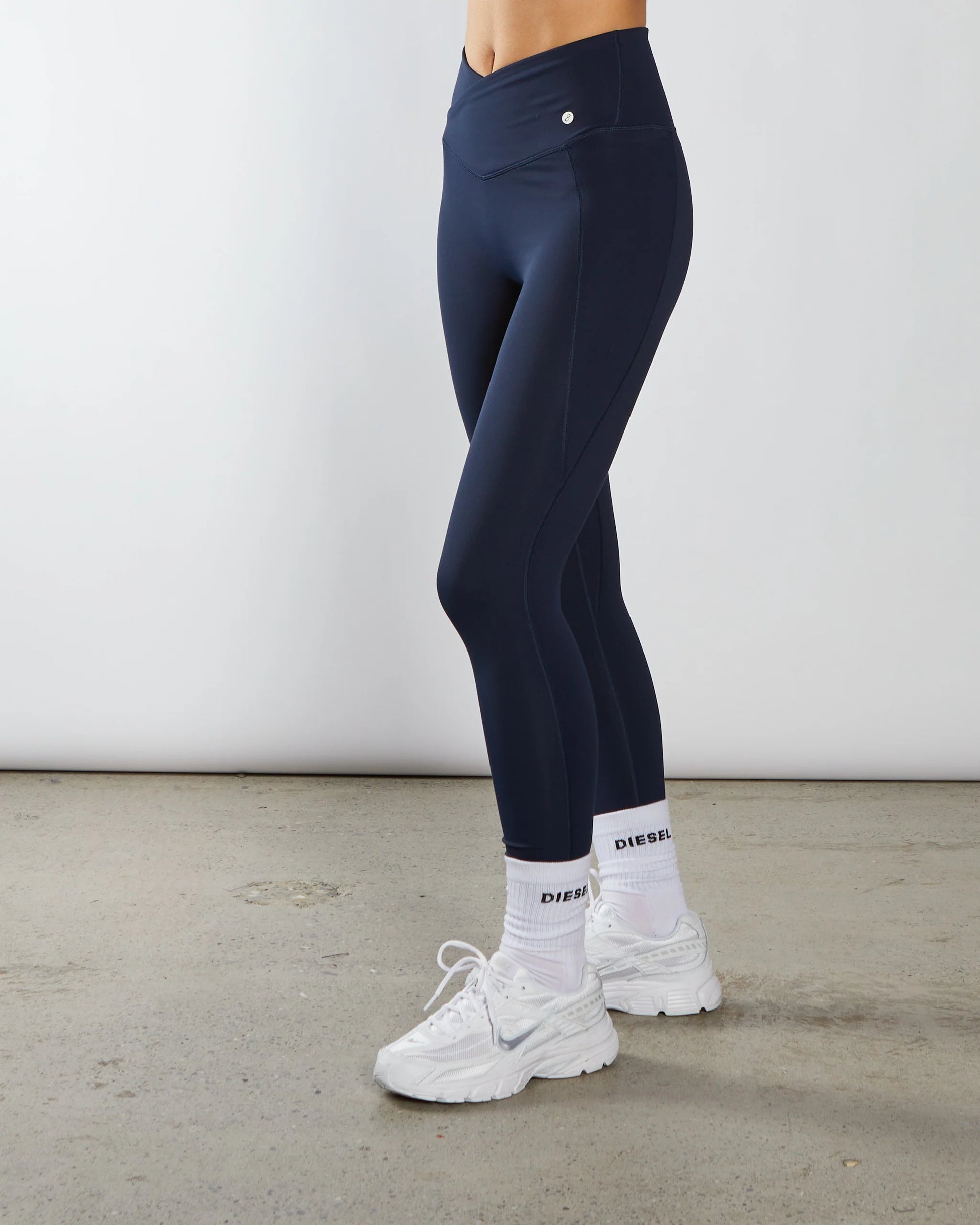 Person wearing navy leggings and white sneakers on a plain background