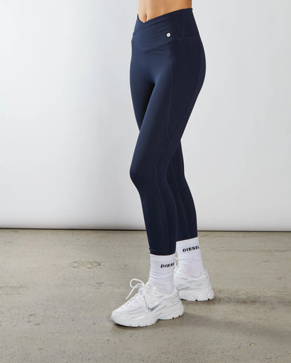 Person wearing navy leggings and white sneakers on a plain background