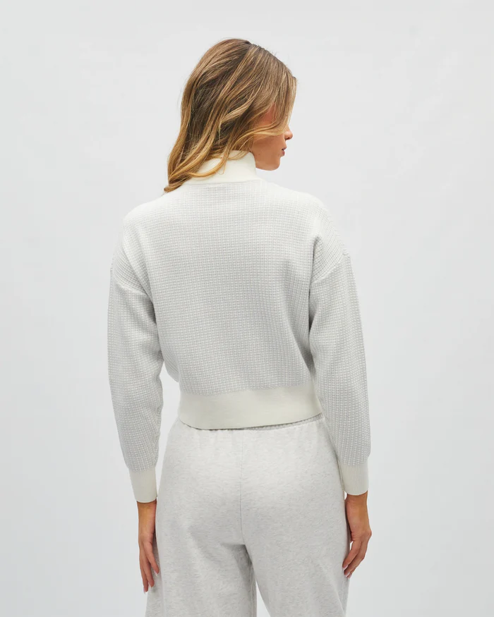 Person wearing a light gray textured sweater and pants on a white background