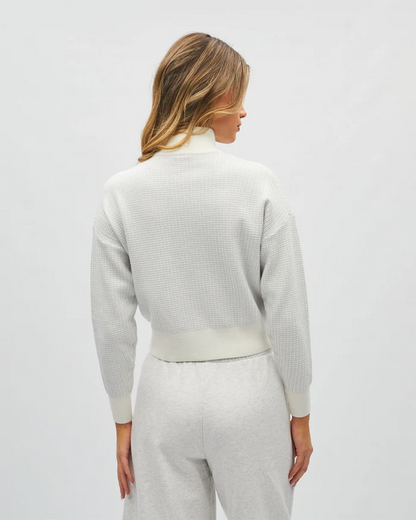 Person wearing a light gray textured sweater and pants on a white background