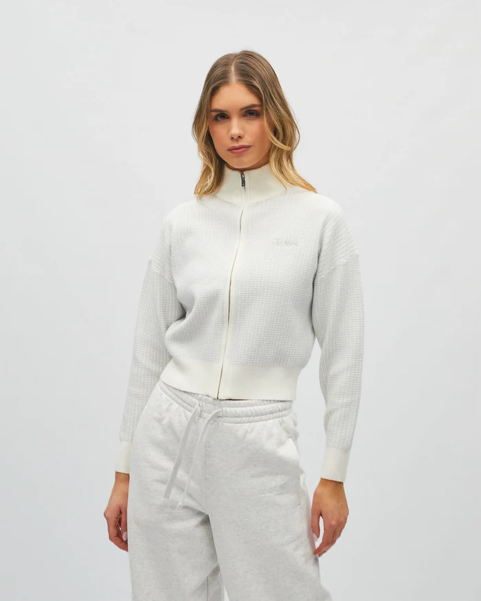 Woman wearing a white zip-up hoodie and gray pants on a light gray background
