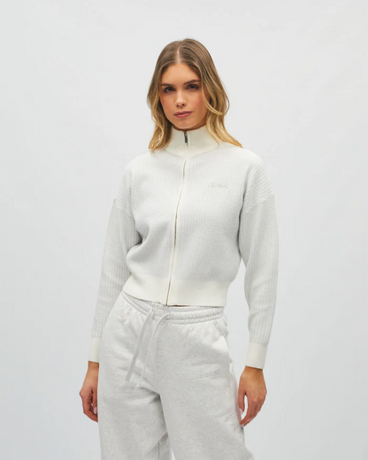 Woman wearing a white zip-up hoodie and gray pants on a light gray background