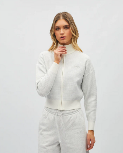 Woman wearing a light gray zip-up sweater and pants on a white background