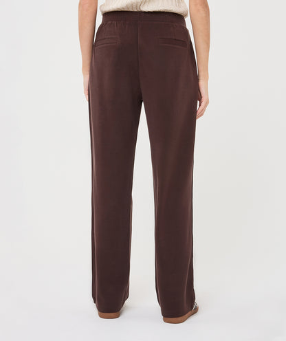 A person shown from the back wearing dark brown wide-leg trousers, photographed against a clean light gray studio background.