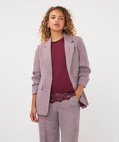 A model wearing a matching lavender-gray textured blazer and trousers set with a burgundy top, photographed against a clean light gray studio background.