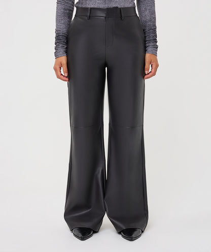 A model is shown from the waist down wearing high-waisted, wide-leg black faux-leather trousers, a gray long-sleeve top, and black pointed-toe heels against a light gray studio background.