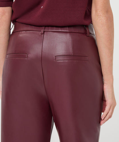 Close-up back view of a person wearing high-waisted burgundy faux-leather trousers with a matching top, against a light gray studio background.