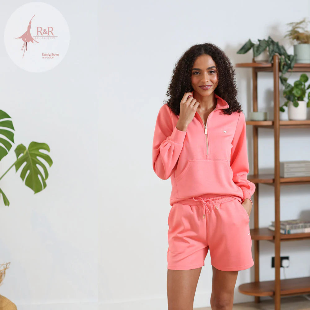 Woman wearing a pink outfit in a room with a plant and shelves.