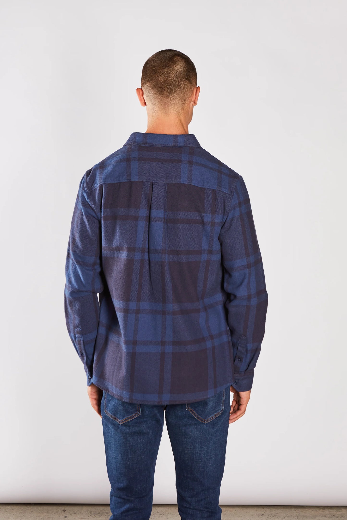 Man wearing a blue plaid shirt and jeans against a white background