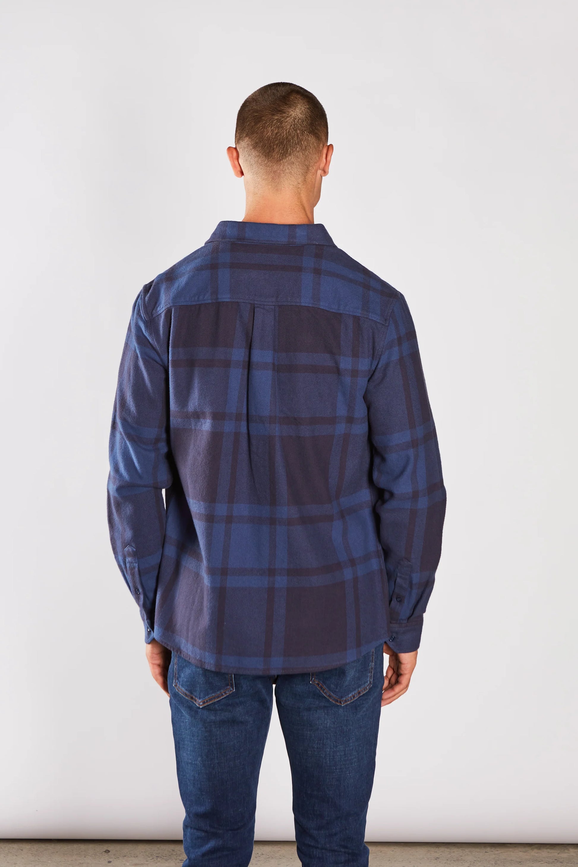 Man wearing a blue plaid shirt and jeans against a white background