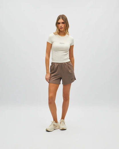 Woman wearing a white t-shirt and brown shorts on a plain background