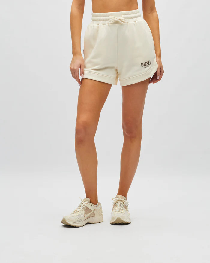Person wearing cream-colored shorts with a brand logo on a plain background