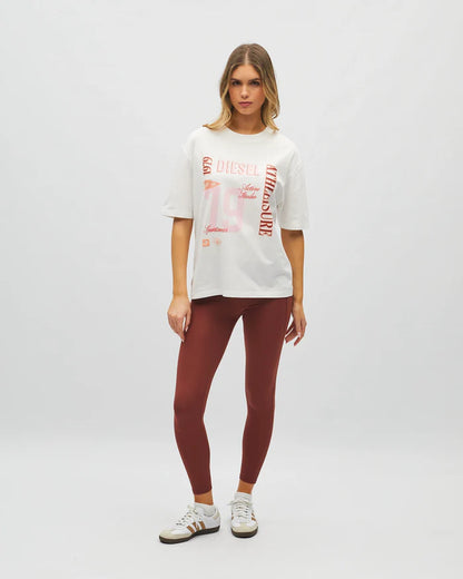 Woman wearing a white graphic t-shirt and maroon leggings on a light gray background