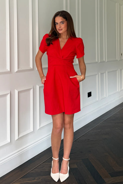 Woman wearing a red dress standing in a room with white paneled walls.