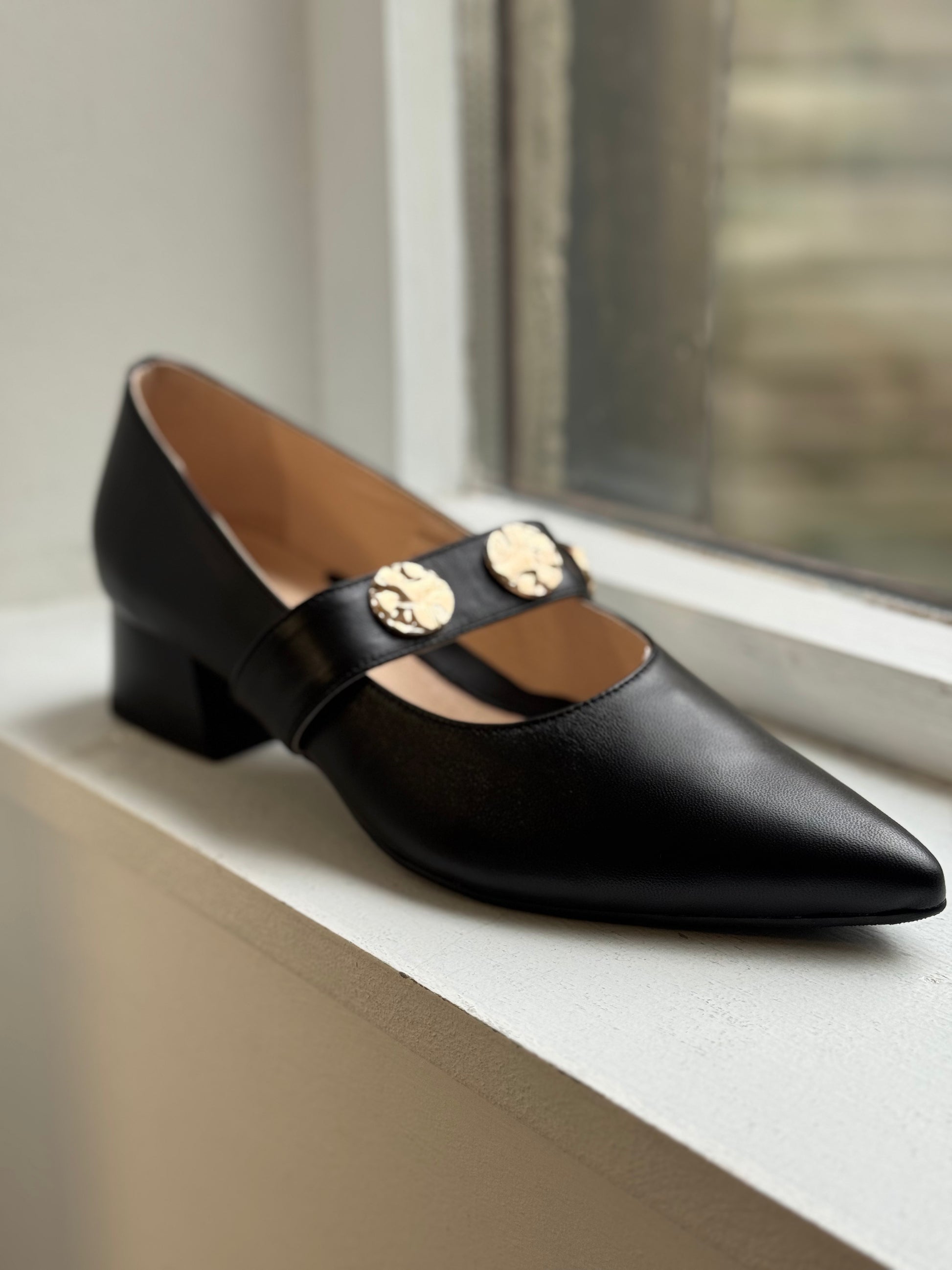 Black shoe with gold accents on a white surface near a window