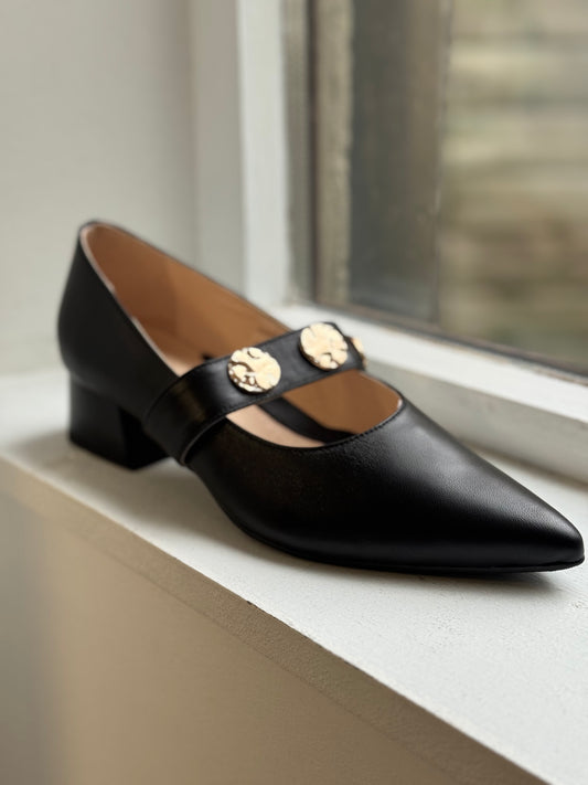 Black shoe with gold accents on a white surface near a window