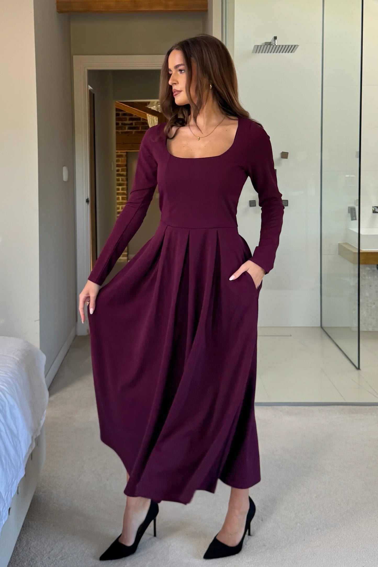Woman wearing a long purple dress in a room with a bed and bathroom.
