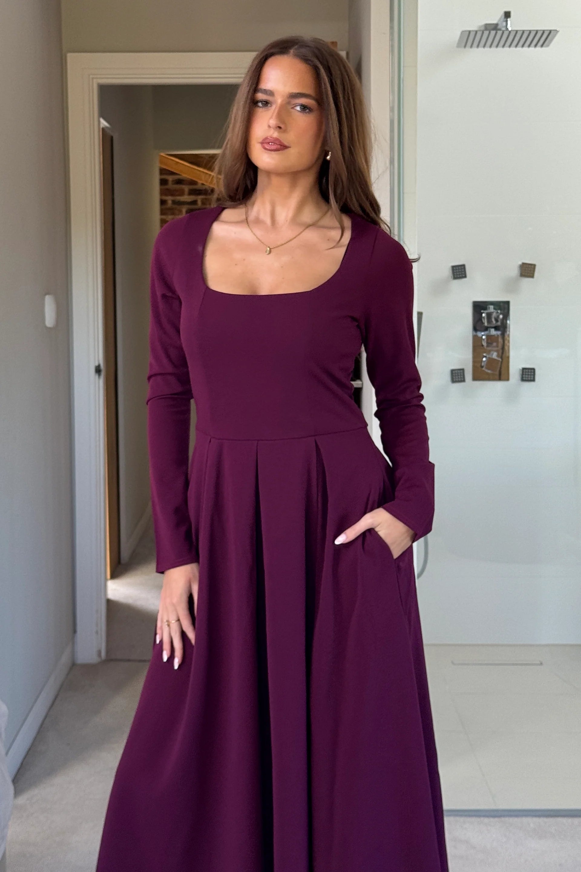 Woman wearing a long purple dress standing in a room with neutral decor.