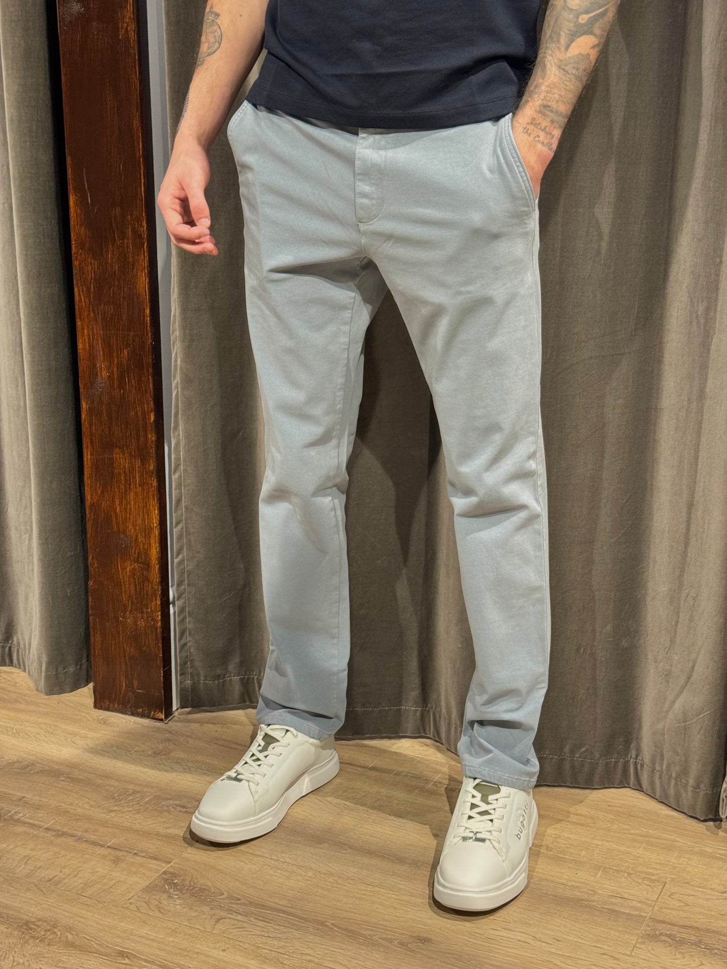 Person wearing light gray pants and white sneakers standing against a curtain background