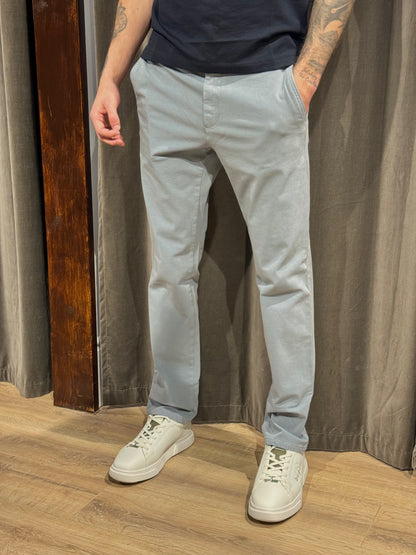 Person wearing light gray pants and white sneakers standing against a curtain background
