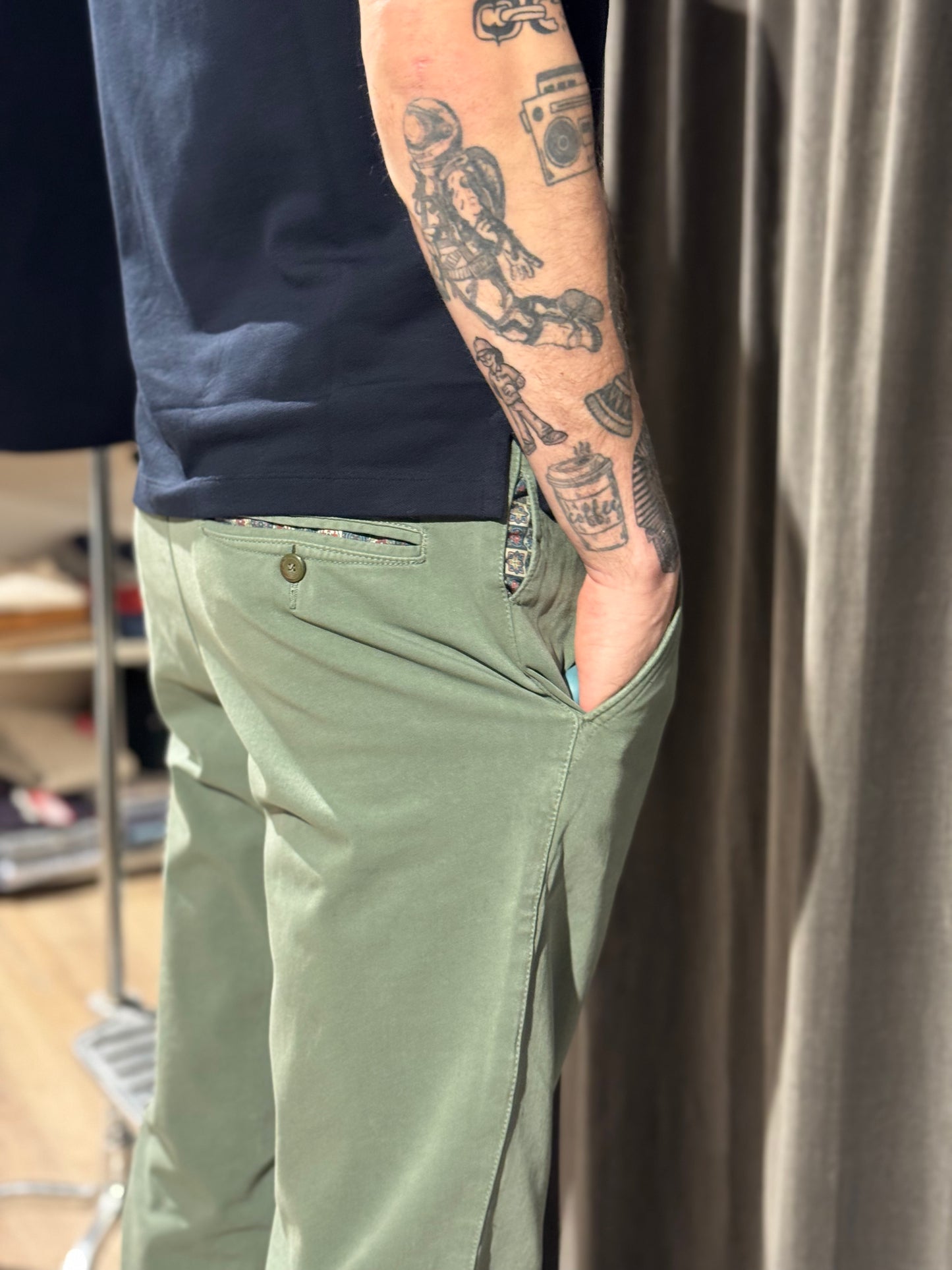 Person wearing green pants with a tattooed arm, standing against a neutral background